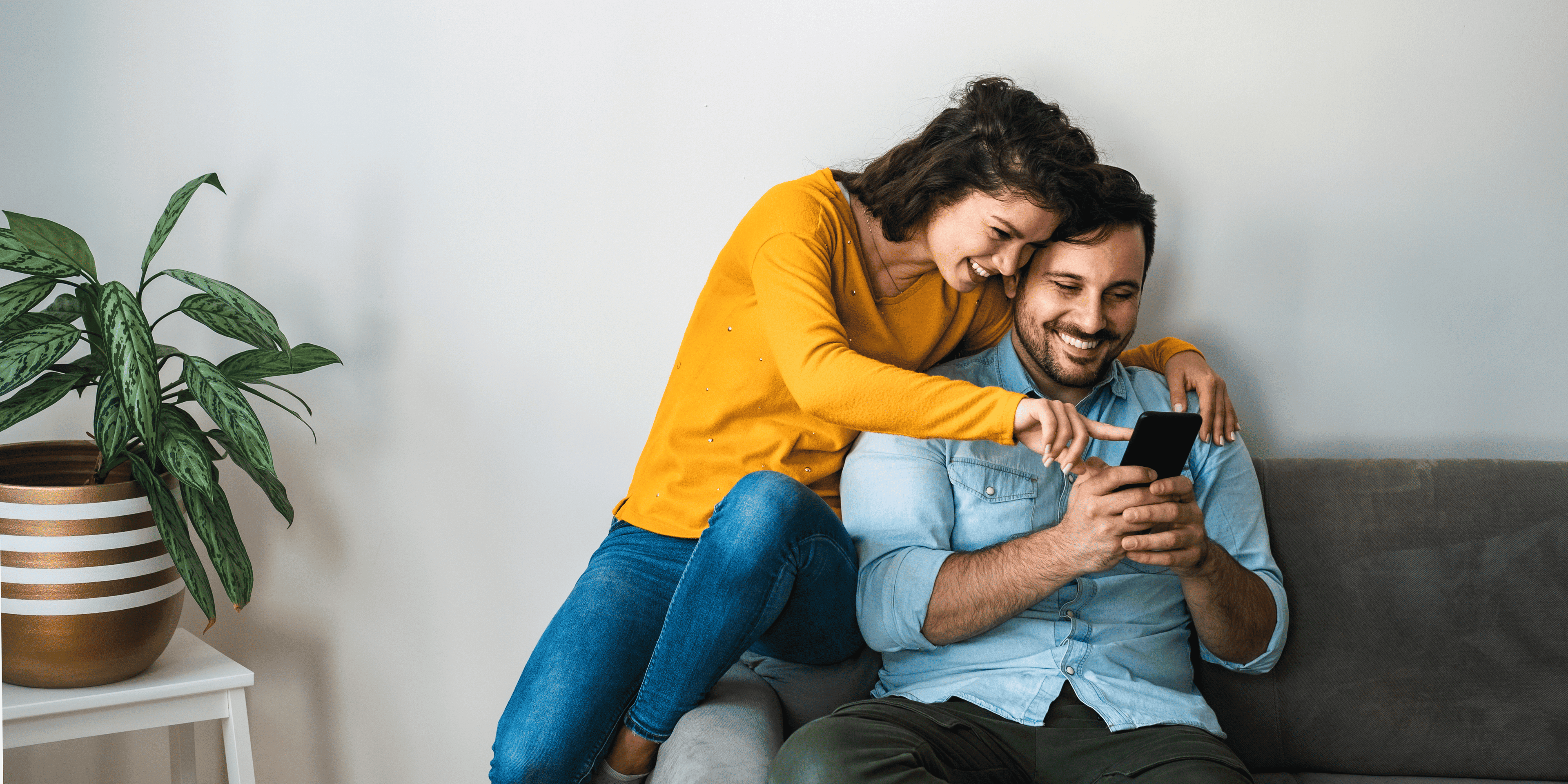 Man and woman sitting on a couch, looking at a phone together.