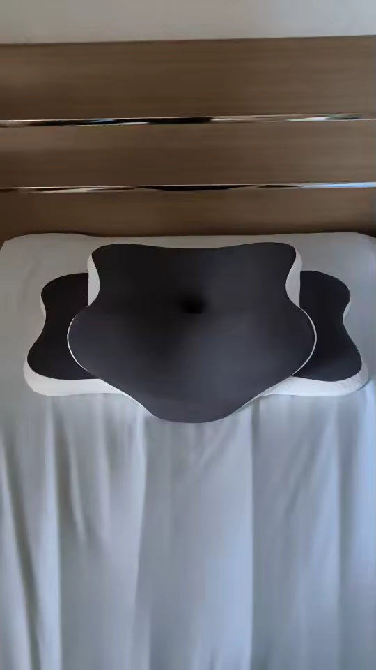 Black massage pillow on a white bed with a wooden headboard.