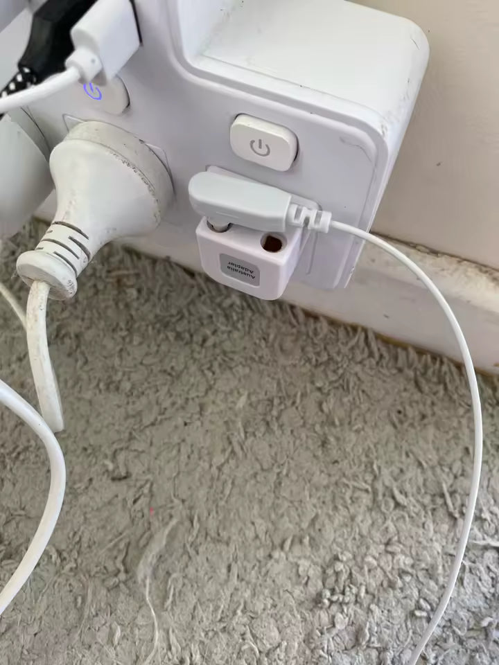White electronic device with multiple cables plugged into it on a textured surface.